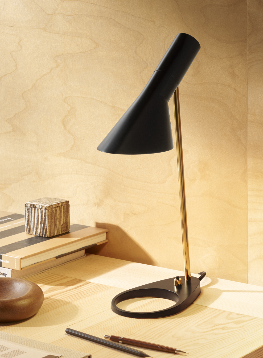 Arne Jacobsen table lamp with sleek black and gold design on a wooden desk, © 2025 Louis Poulsen.