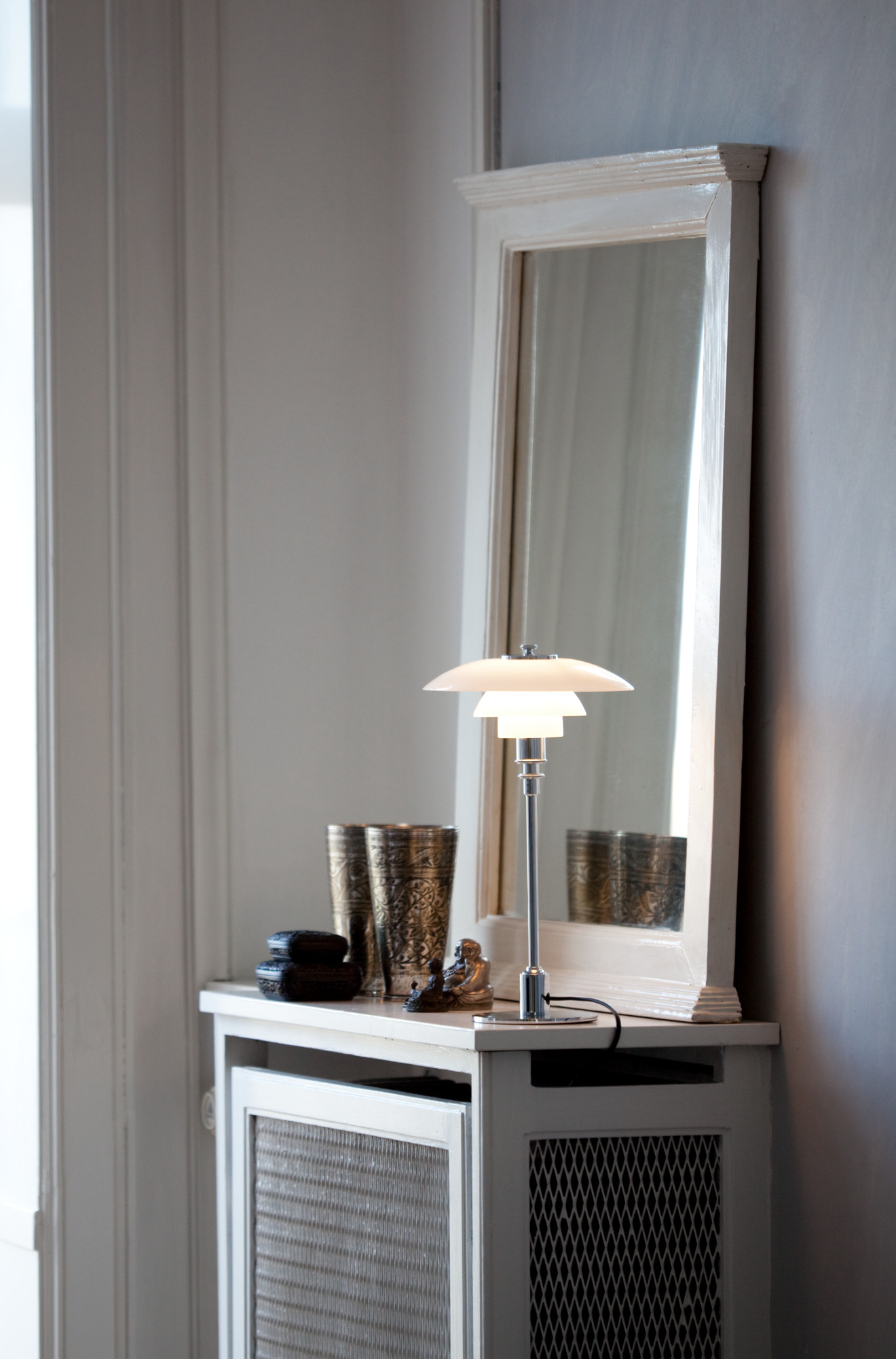 PH 2/1 table lamp on a cabinet, beside a mirror with decorative items, © 2025 Louis Poulsen.