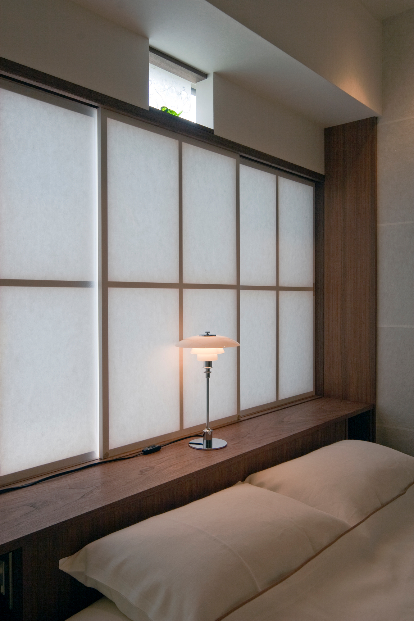 PH 2/1 table lamp on a nightstand, with soft light casting on the wall, © 2025 Louis Poulsen.