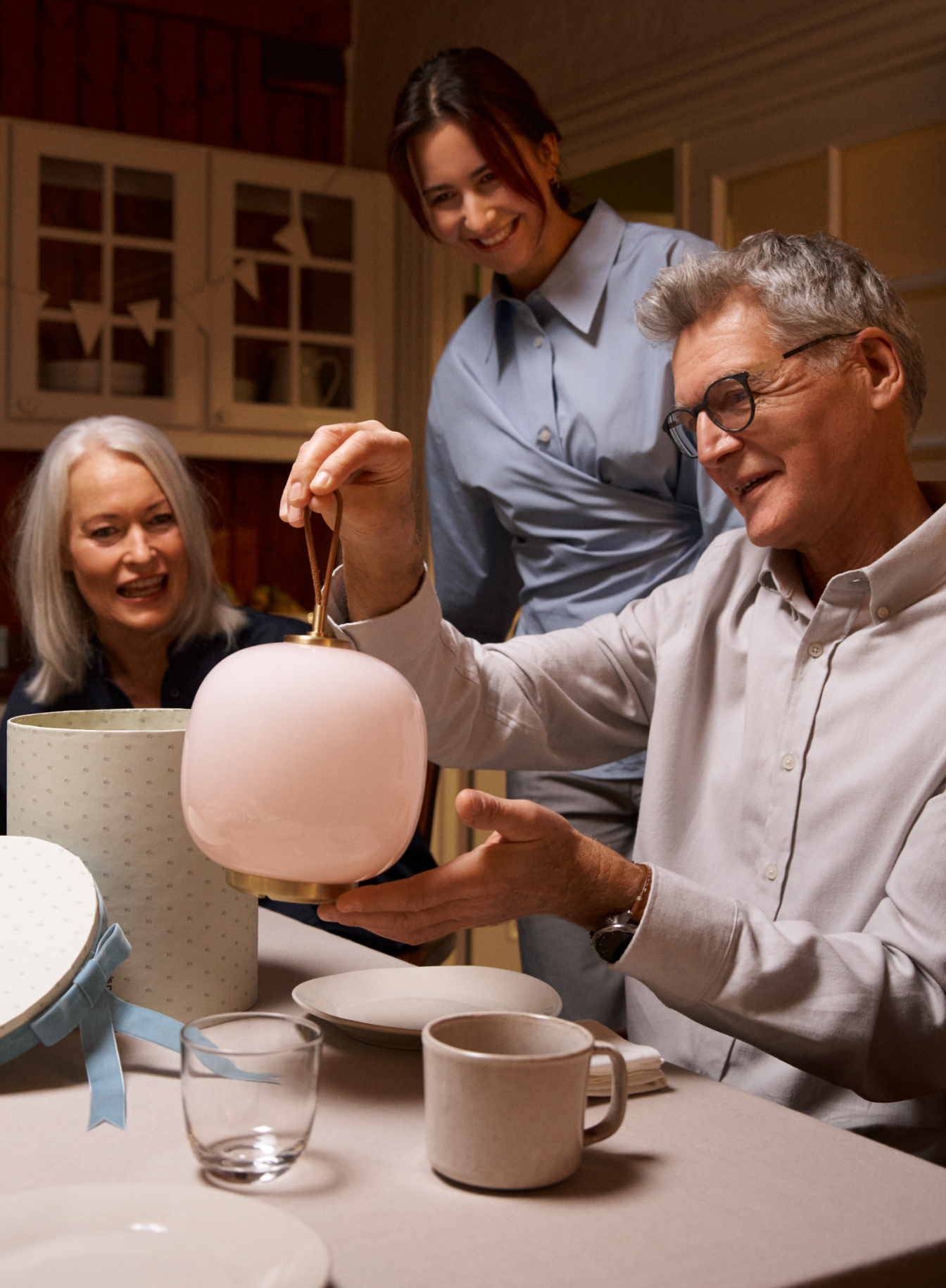 Man unboxing a vl 45 portable lamp at a festive table with smiling onlookers, © 2025 Louis Poulsen.