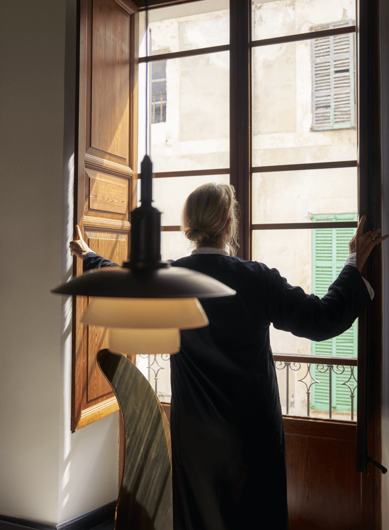 PH Aged Brass Opal pendant lamp illuminating a person opening a window, © 2025 Louis Poulsen.