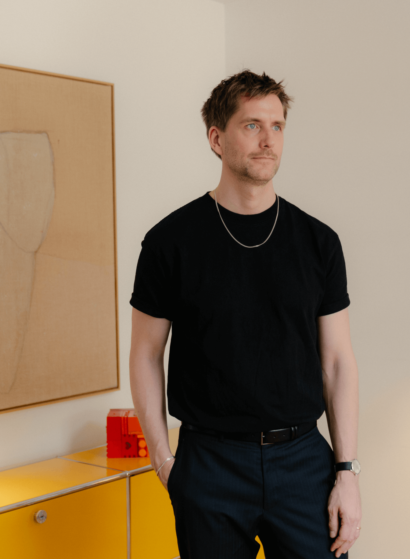 Sigurd Larsen standing by a yellow cabinet with artwork in background, © 2025 Louis Poulsen.