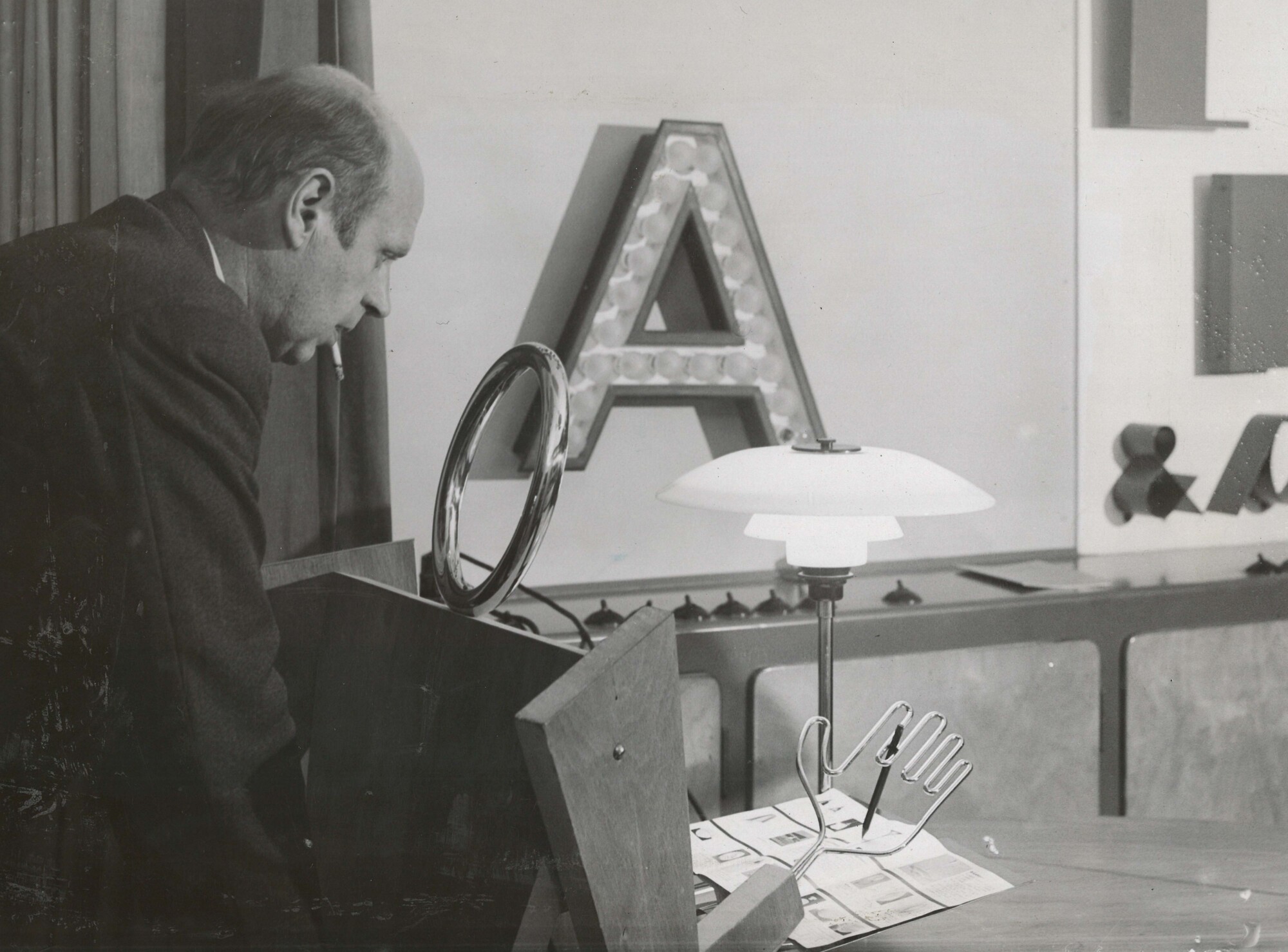 Poul Henningsen observa una lámpara PH de mesa temprana en showroom, © 2025 Louis Poulsen.