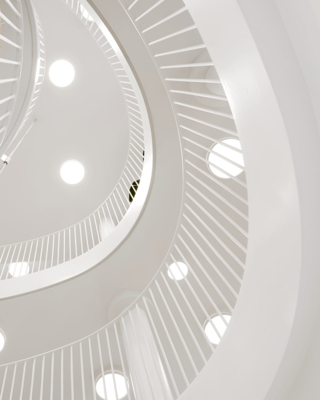 Recessed ceiling lights following curved stairway architecture, © 2025 Louis Poulsen.